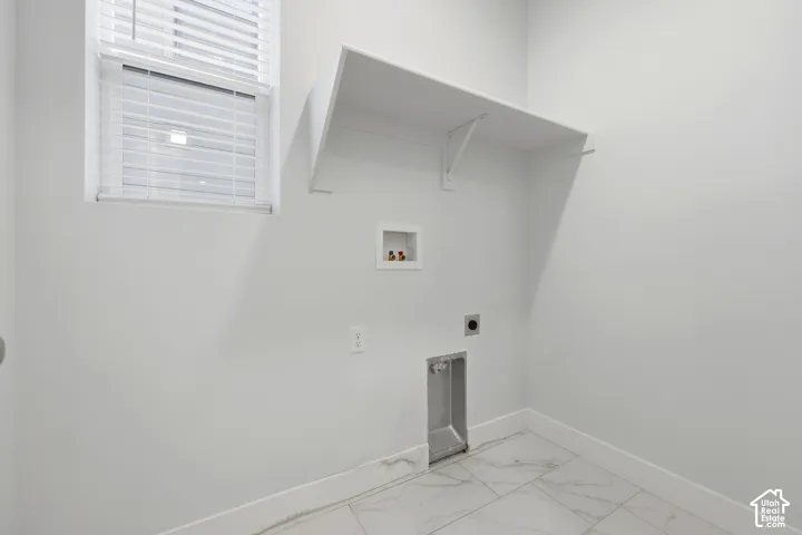 White interior walls, overhead shelving, window with blinds, plumbing hookups, and large format tiled flooring