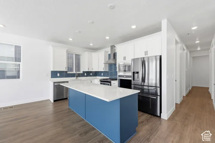 Kitchen featuring a blue accent island, stainless steel appliances, white cabinetry, a blue subway tile backsplash, and wood-finish flooring