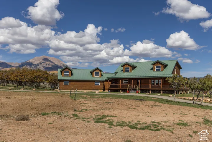 Log cabin exterior with a green metal roof, multiple dormer windows, and a raised porch