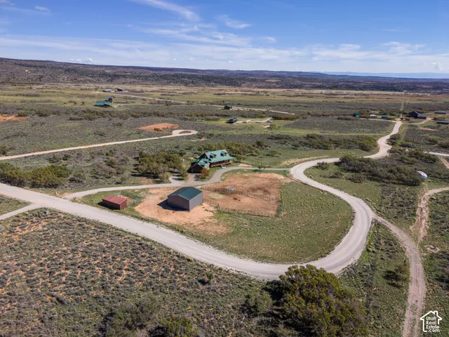 Expansive rural property featuring a main residence with a green roof, a detached metal outbuilding, a fenced enclosure, and a network of unpaved roads
