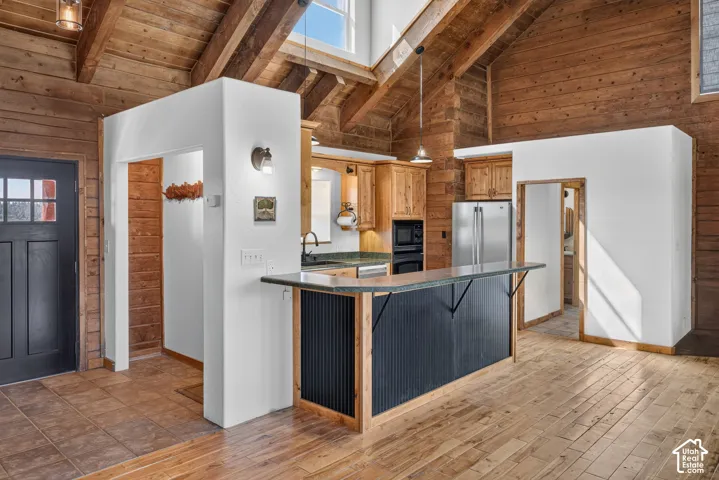 Wood-finish flooring throughout, vaulted wood-paneled ceilings, skylight, kitchen island with breakfast bar seating, and stainless steel appliances