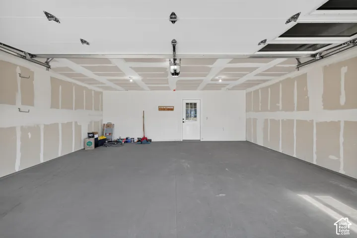 Spacious garage featuring a durable gray floor finish, exposed ceiling joists, recessed lighting, and a white entry door with glass panels