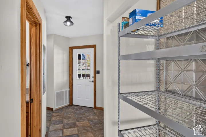 Galvanized metal shelving with a patterned metal back panel, a white door with multiple glass panes, wood trim, brown and tan floor tiles, and a semi-flush mount ceiling light