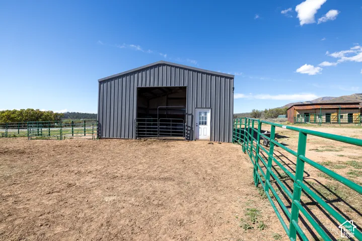 Metal-sided barn structure with open stalls, secondary exterior building, and perimeter fencing
