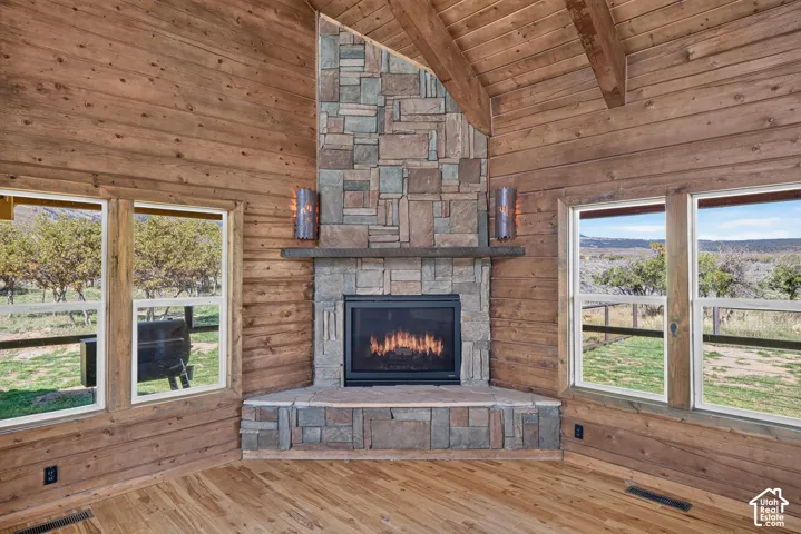 Corner great room showcasing stacked stone fireplace with gas insert, wood-beamed ceiling, and hardwood flooring