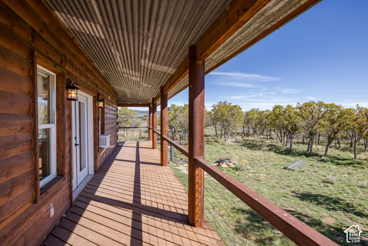 Expansive wood-finish deck with a corrugated metal ceiling and wood-finish railing overlooking a wooded landscape
