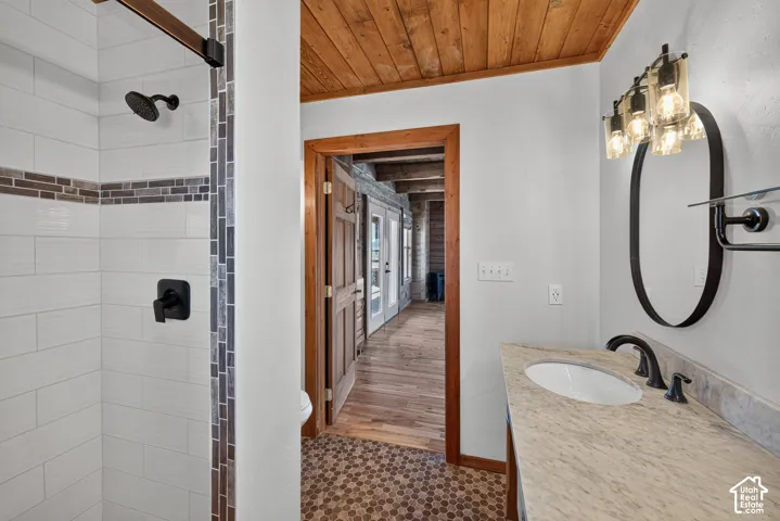Shower with white subway tile and decorative accent band, matte black fixtures, wood-finish ceiling, oval mirror, and vanity with undermount sink