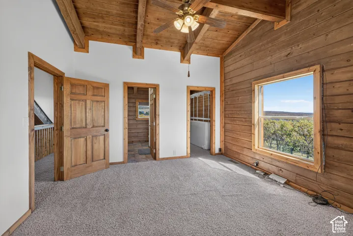 Spacious primary suite featuring vaulted wood-beam ceilings, exposed wood-finish walls, and abundant natural light from large picture windows