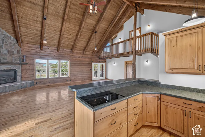 Vaulted wood-plank ceilings, wood-finish flooring, stone-clad fireplace with mantel, wood cabinetry with dark hardware, and a built-in cooktop