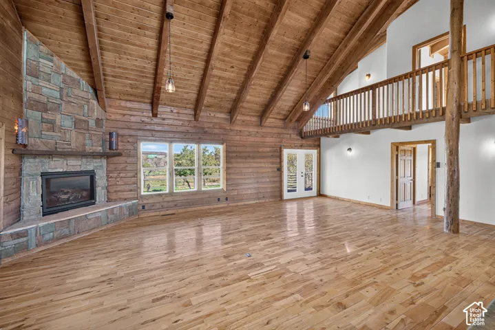 Vaulted wood-paneled ceilings, stone-clad fireplace with mantel, exposed wood beams, wood-finish flooring, and a second-level wood railing