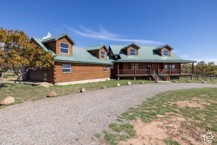 Wood-sided residence with multiple dormer windows, a green metal roof, and a gravel driveway