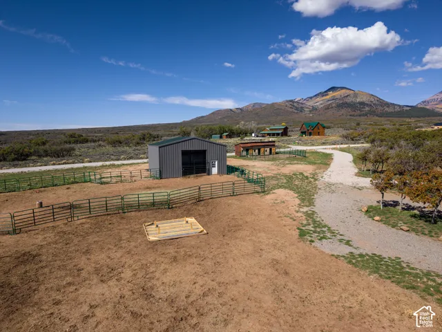 Expansive property featuring a detached metal-sided barn, gravel driveway, and surrounding green fencing, set against a mountainous backdrop