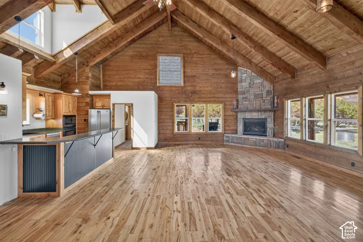 Vaulted wood-finish ceilings with exposed beams, wood-finish flooring, stone fireplace, and a kitchen island with built-in appliances