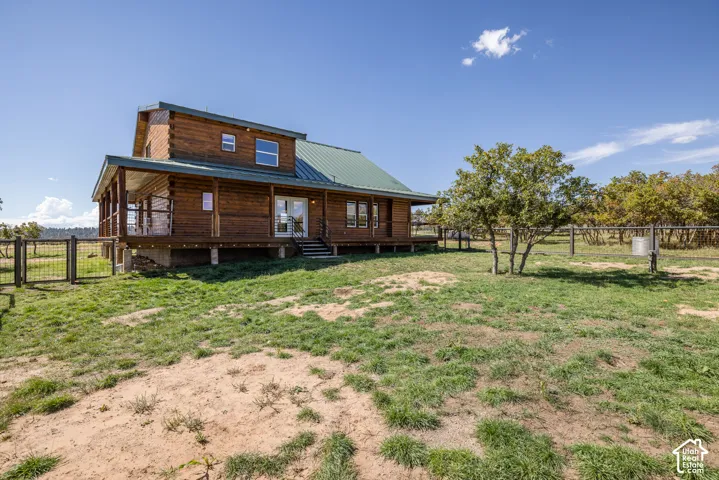 Log cabin exterior with a green metal roof, elevated covered porch, and a fenced perimeter
