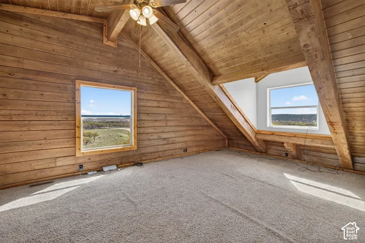 Vaulted wood-paneled ceilings with exposed wood beams, wall-to-wall carpeting, and multiple windows providing natural illumination