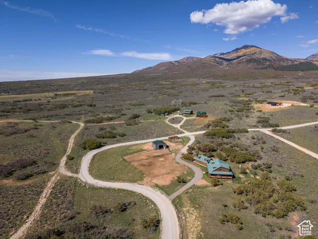 Expansive rural landscape featuring a single-story dwelling with a green roof, dirt roads, and multiple outbuildings
