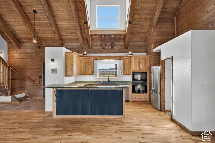 Open-concept kitchen featuring wood-finish flooring, natural wood cabinetry, stainless steel appliances, and a central island with a beaded panel