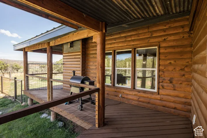 Rustic log cabin exterior with expansive covered deck featuring wood-finish flooring, support columns, and corrugated metal roof overhang