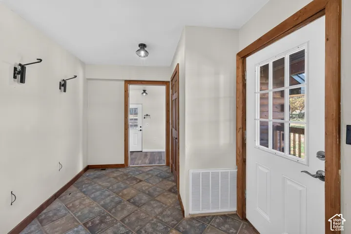 Entryway featuring multi-toned square tile flooring, a white paneled door with divided light windows, and natural wood trim