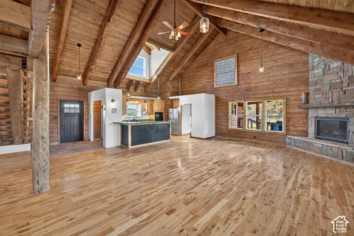 Vaulted wood-paneled ceilings with exposed beams, natural wood flooring, a stone-faced fireplace, a kitchen island with seating, and a skylight