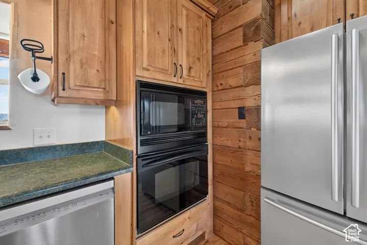 Wood-finish cabinetry, integrated stainless steel appliances, dark green countertops, and wood plank wall finishes