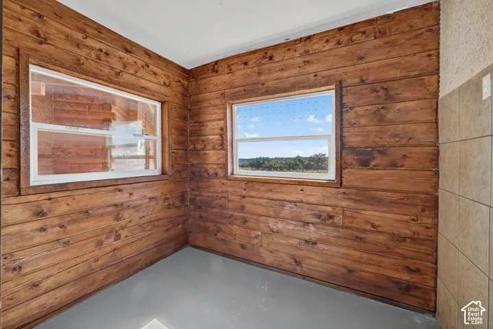 Wood-paneled interior walls, two distinct windows, tiled wall section, painted concrete flooring, and a white ceiling
