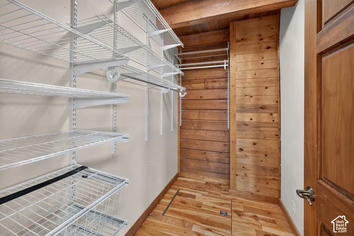 Adjustable wire shelving system, wood-finish flooring, wood-paneled wall, exposed wood ceiling beams, and a wood-finish door with brushed nickel hardware