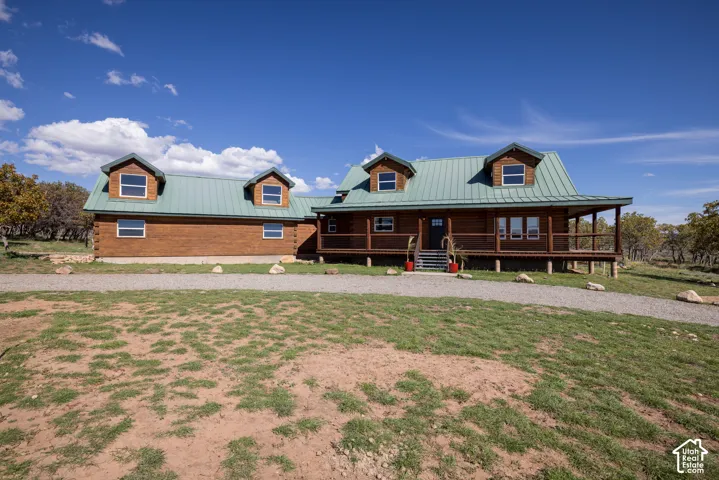 Log cabin exterior with a green metal roof, multiple dormer windows, and a full-length covered porch