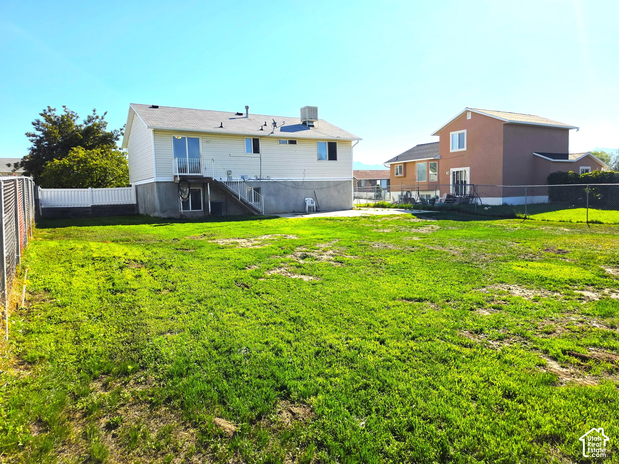 Expansive backyard featuring a chain-link perimeter fence, white vinyl fence, and a concrete patio