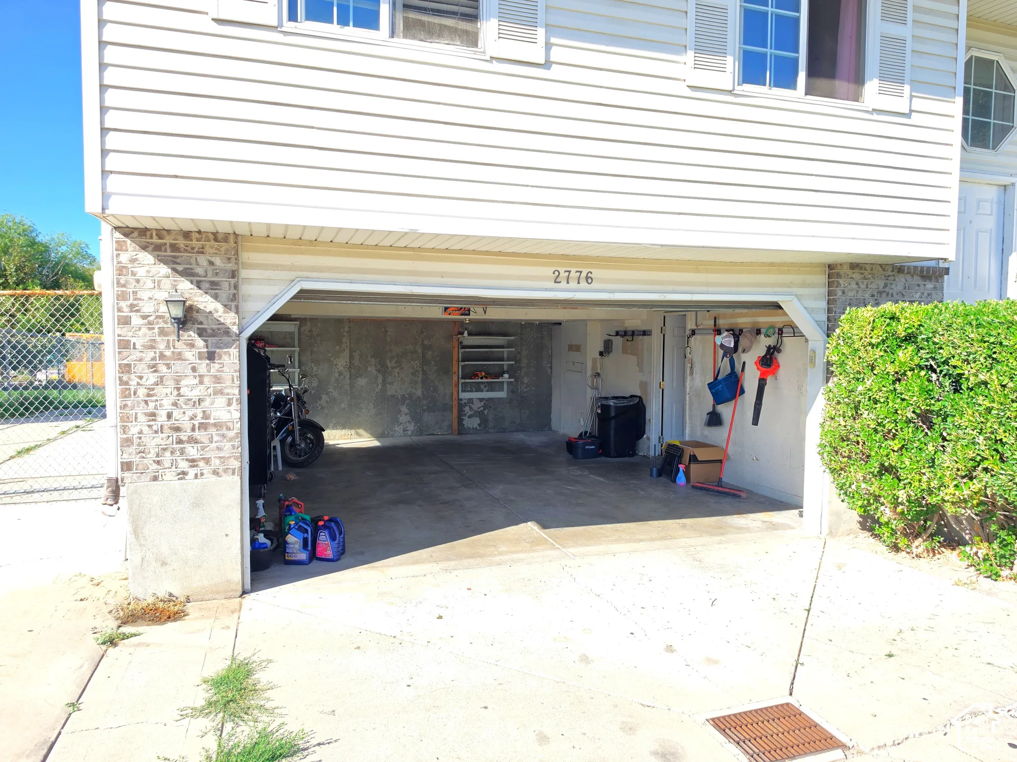 Attached two-car garage with concrete flooring and exposed concrete walls, featuring exterior vinyl siding and brick detailing, with a street number visible above the garage door