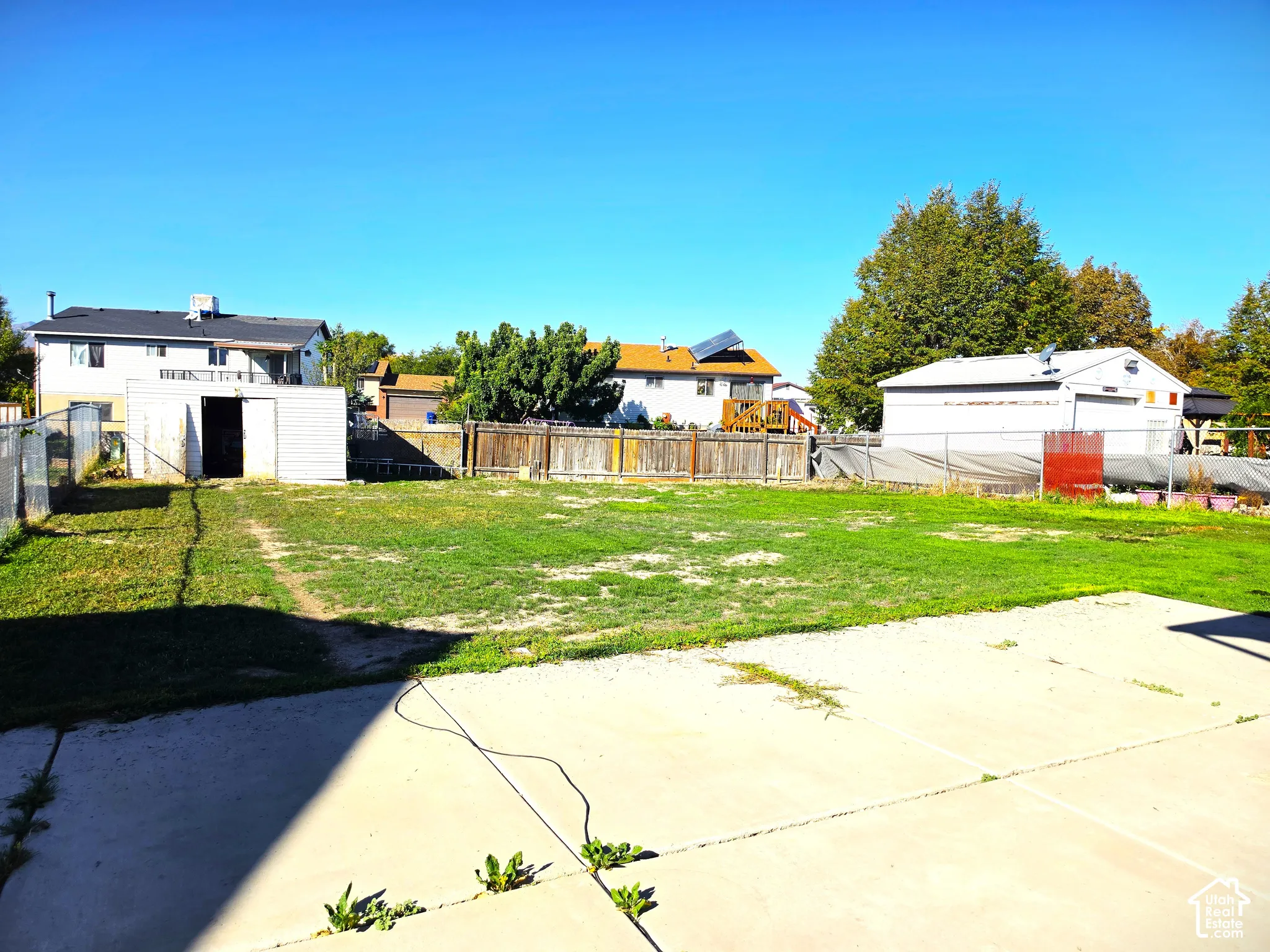 Expansive concrete patio with a large grassy area, a storage shed, and perimeter fencing