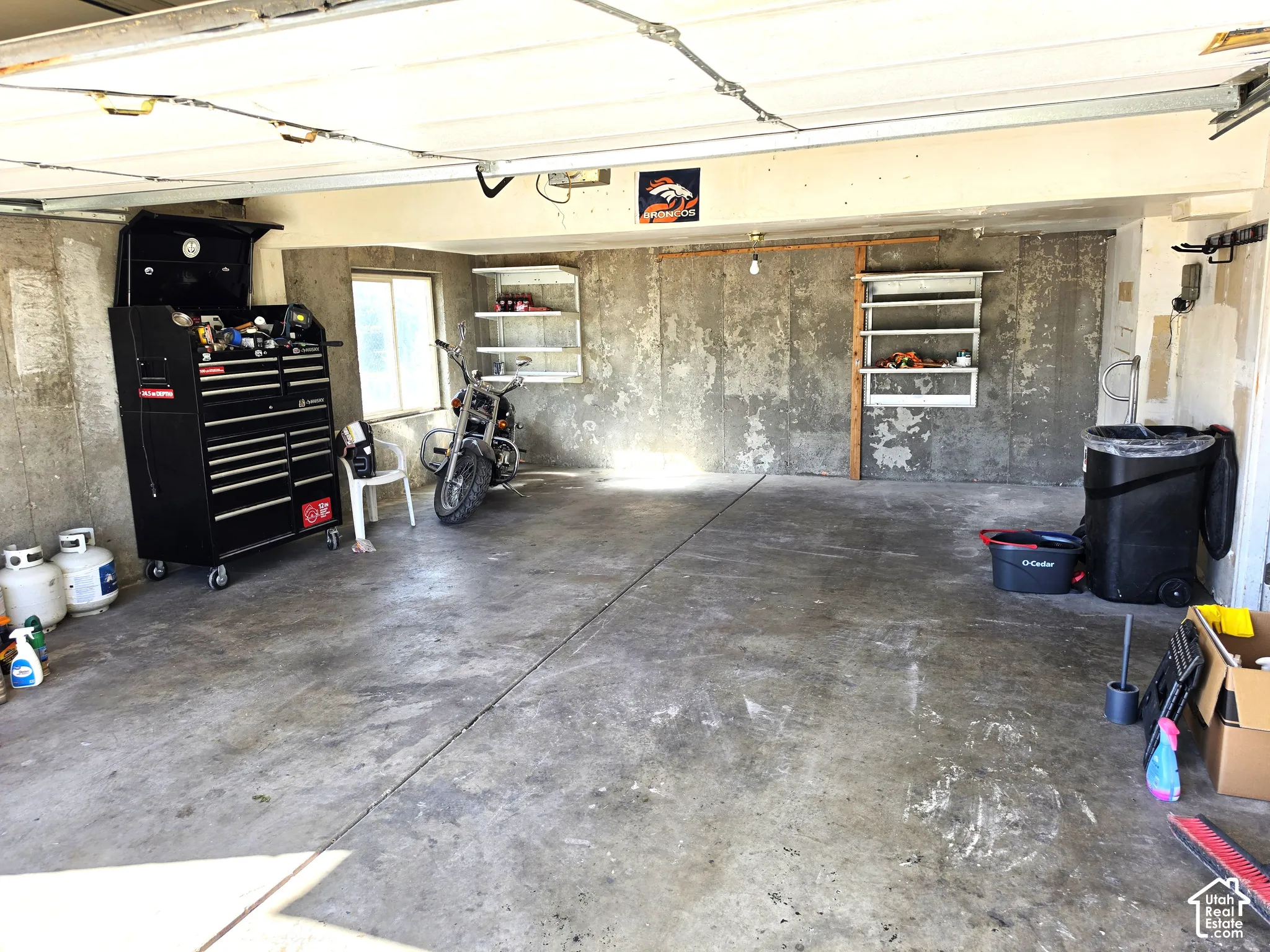 Concrete flooring with a window, wall-mounted shelving units, and exposed ceiling joists
