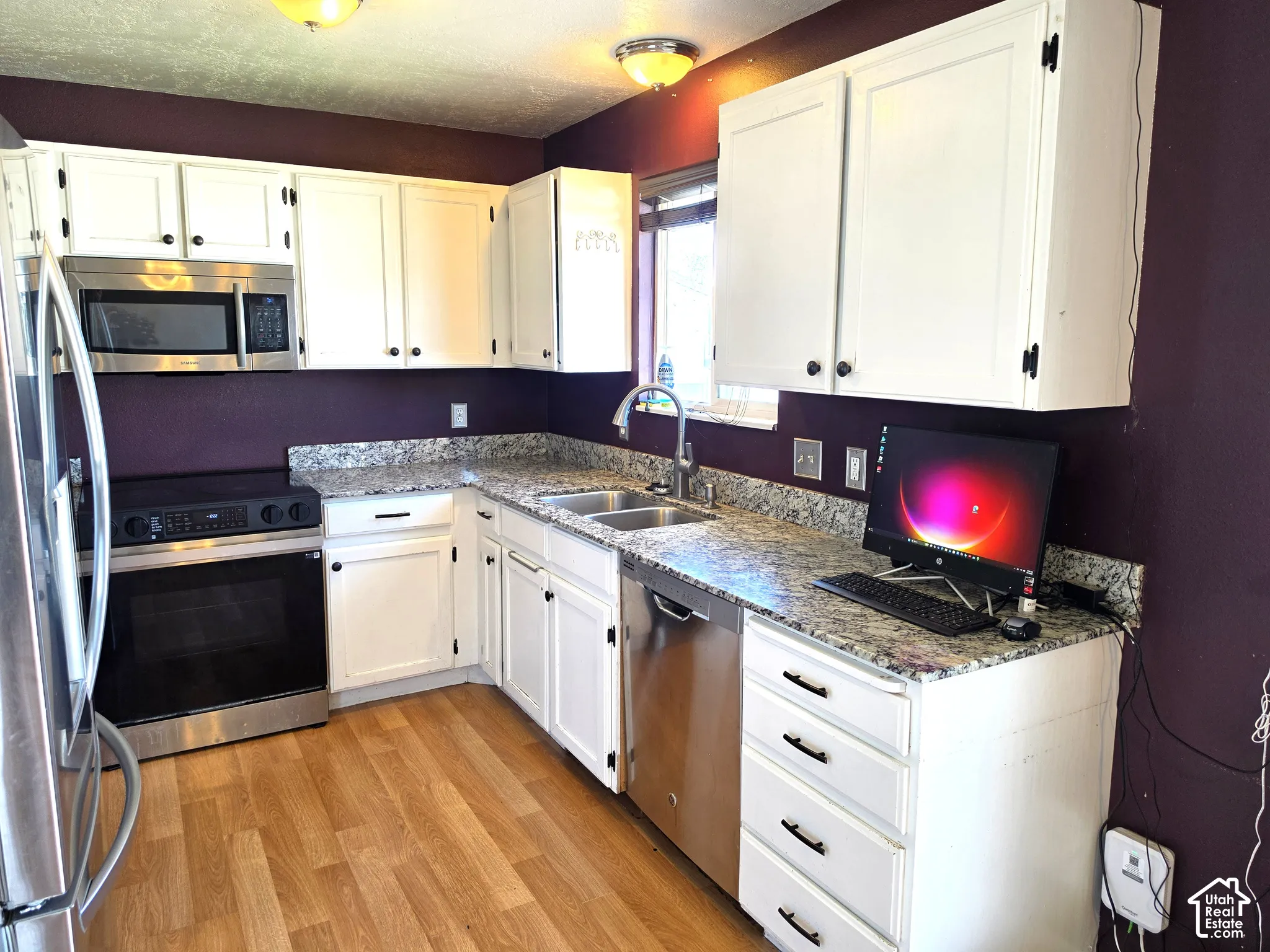 White cabinetry with black hardware, wood-finish flooring, stainless steel appliances, and a double basin sink