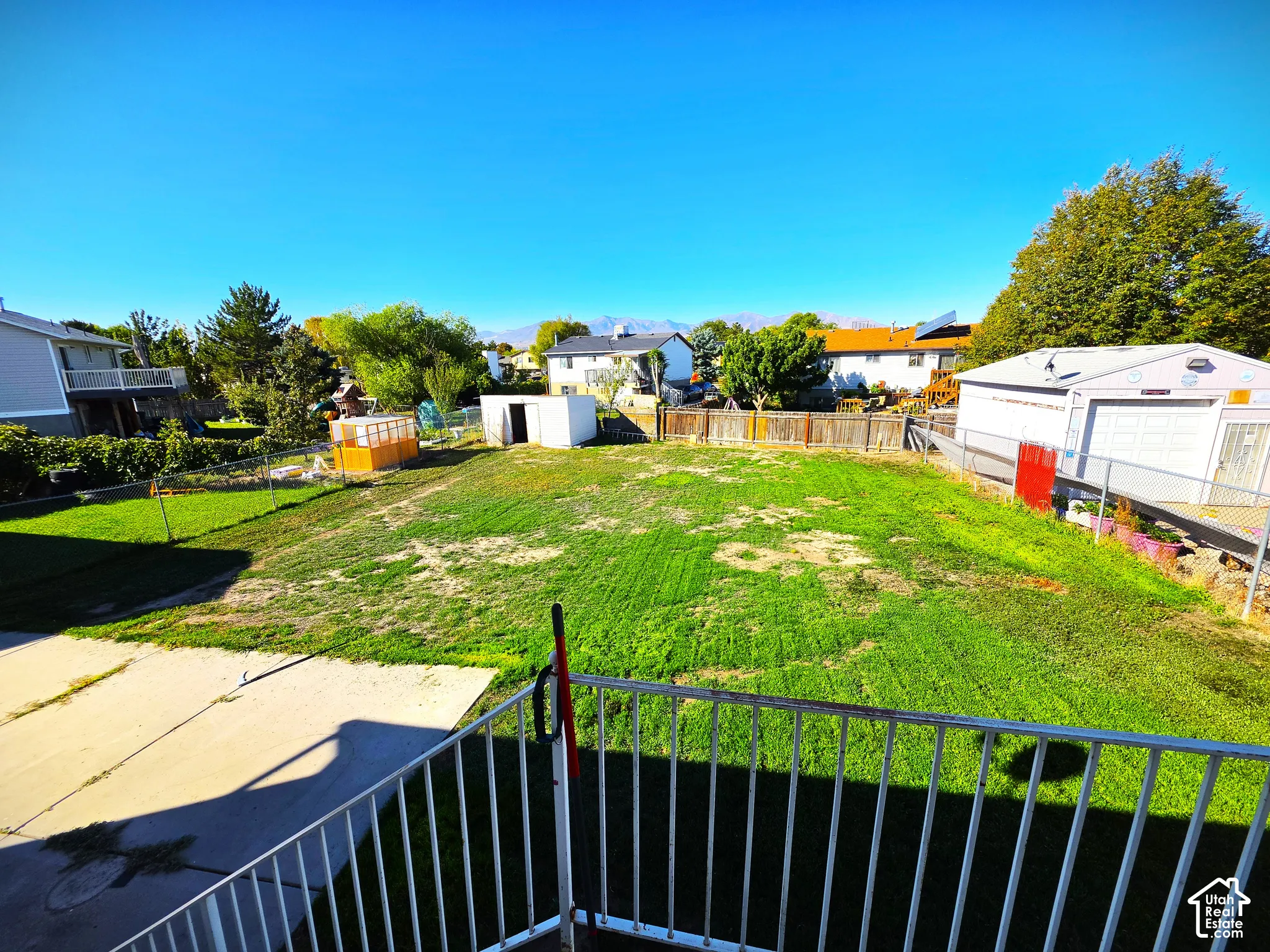 Expansive backyard featuring a large grass area, concrete patio, and a storage shed