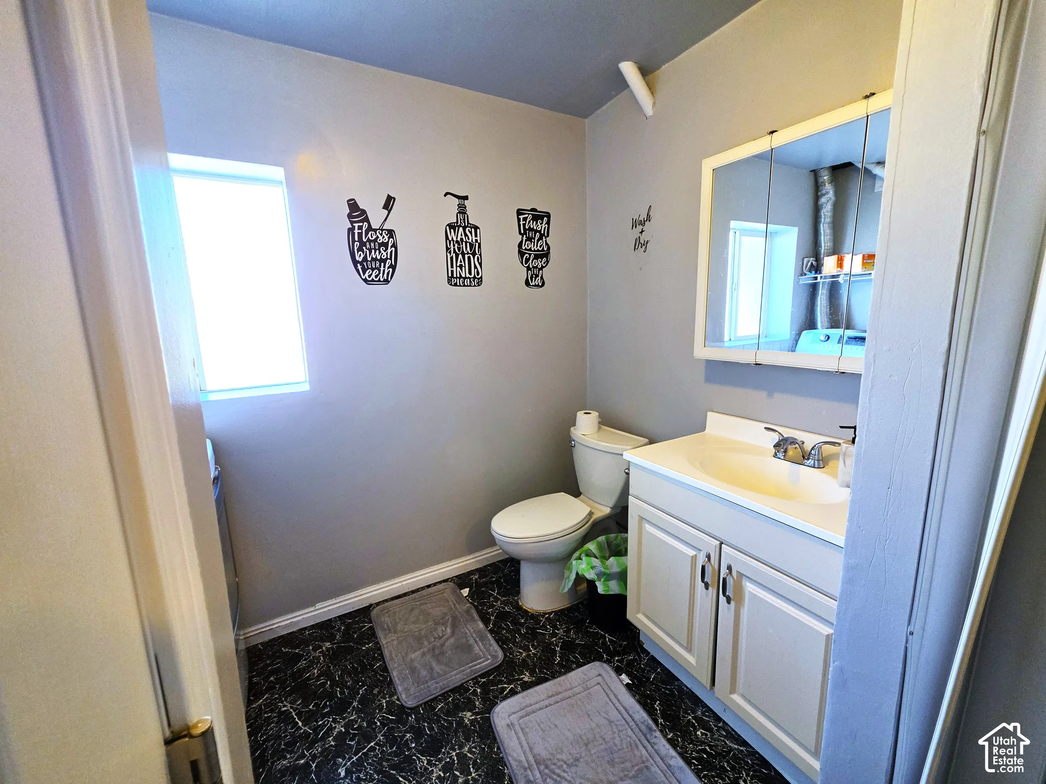 Compact bathroom featuring a window, white vanity with integrated sink, chrome faucet, white medicine cabinet, and dark-toned flooring