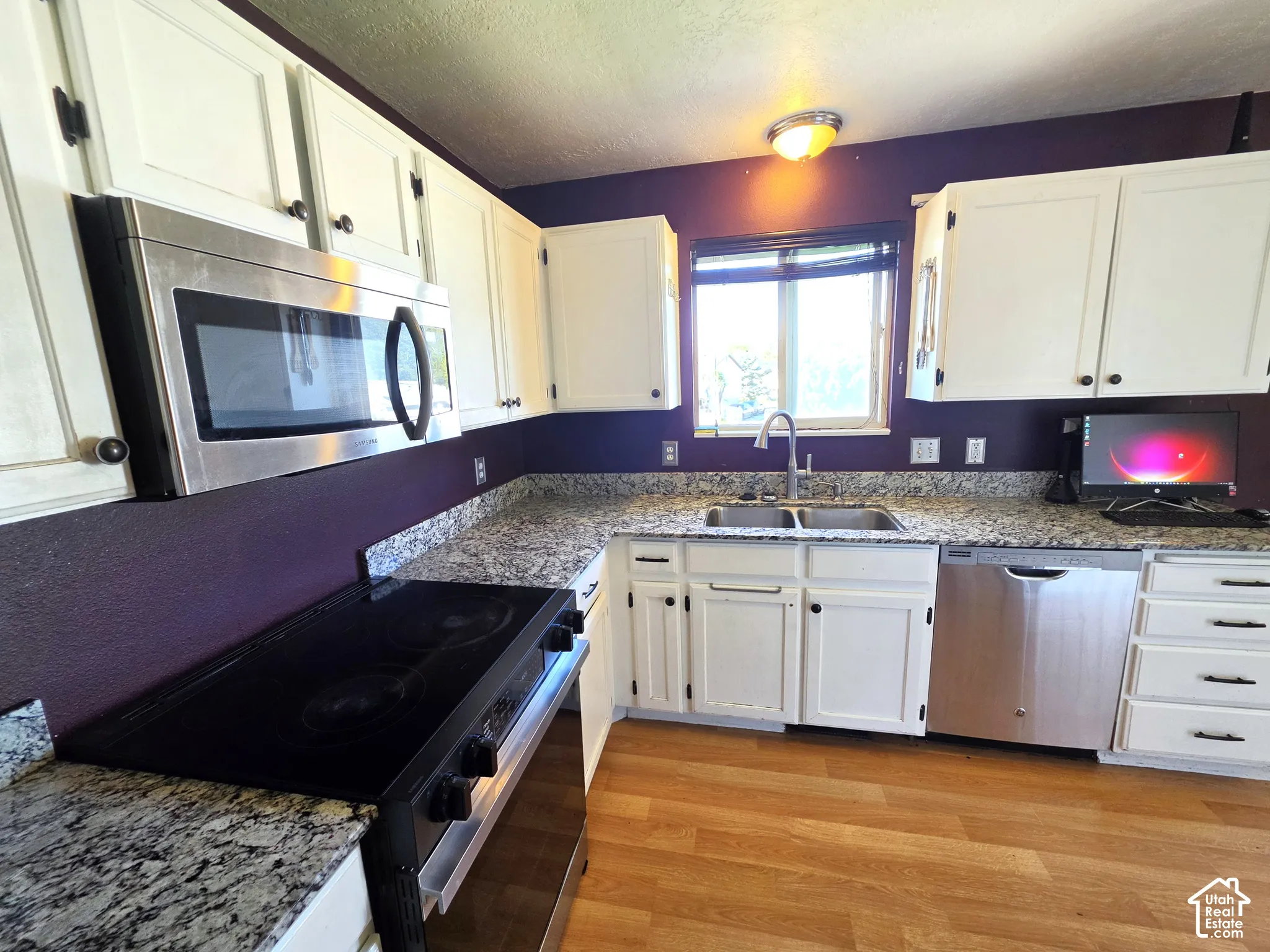 Kitchen featuring white cabinetry, speckled countertops, stainless steel appliances, and wood-finish flooring