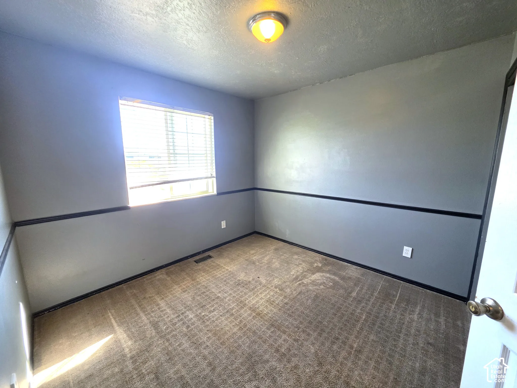 Neutral gray walls with a decorative black trim, complemented by a window featuring horizontal blinds, and a durable carpeted floor