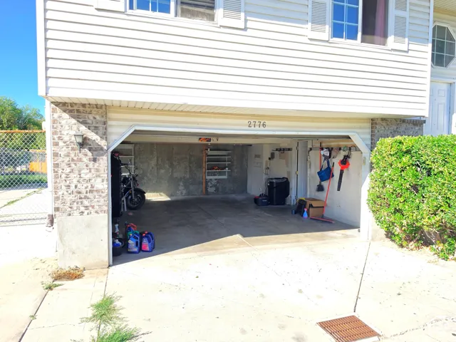 Attached two-car garage with concrete flooring and exposed concrete walls, featuring exterior vinyl siding and brick detailing, with a street number visible above the garage door