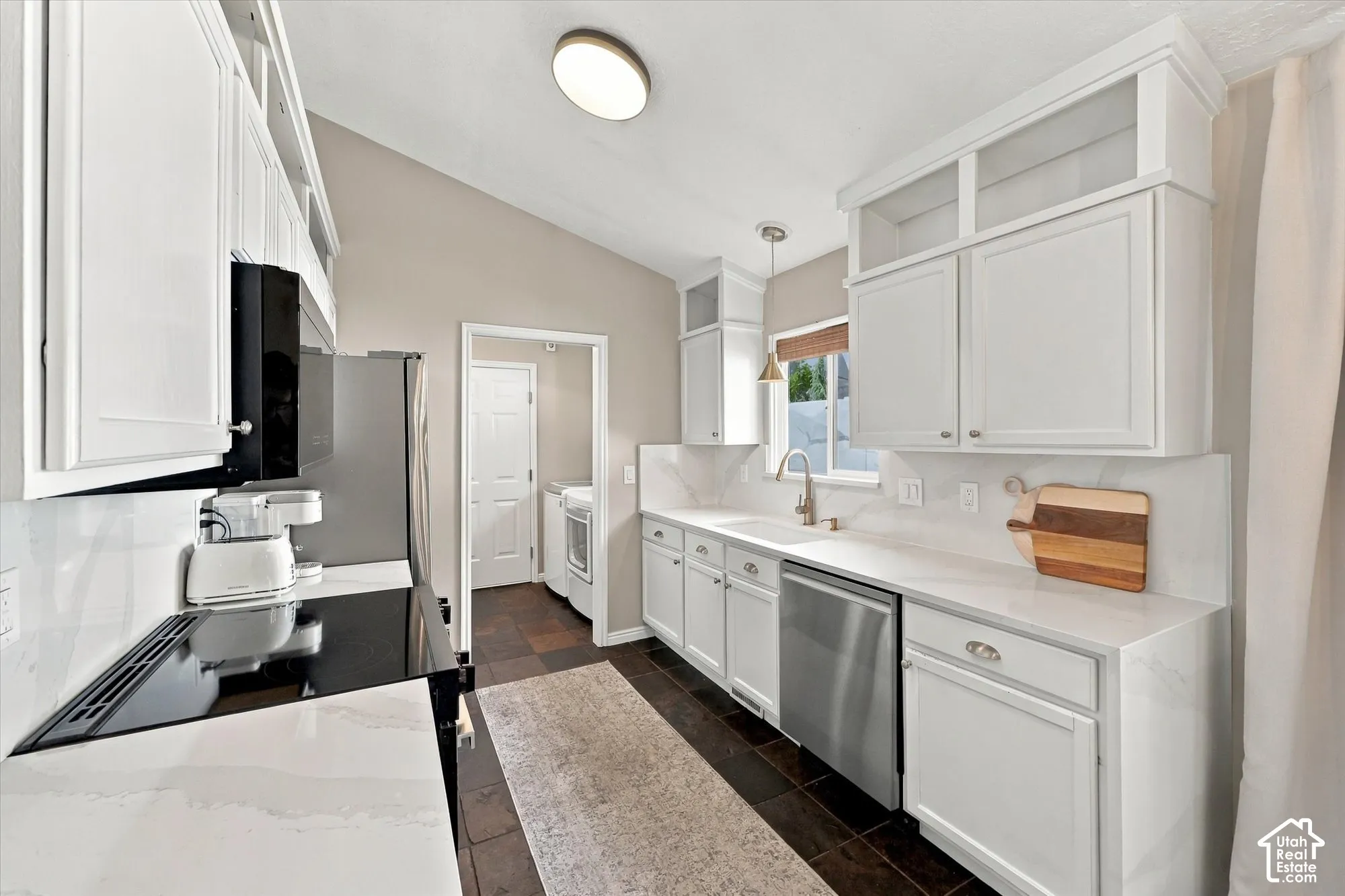 Kitchen featuring white cabinetry, light-toned countertops, a stainless steel dishwasher, a built-in microwave, and dark-toned flooring