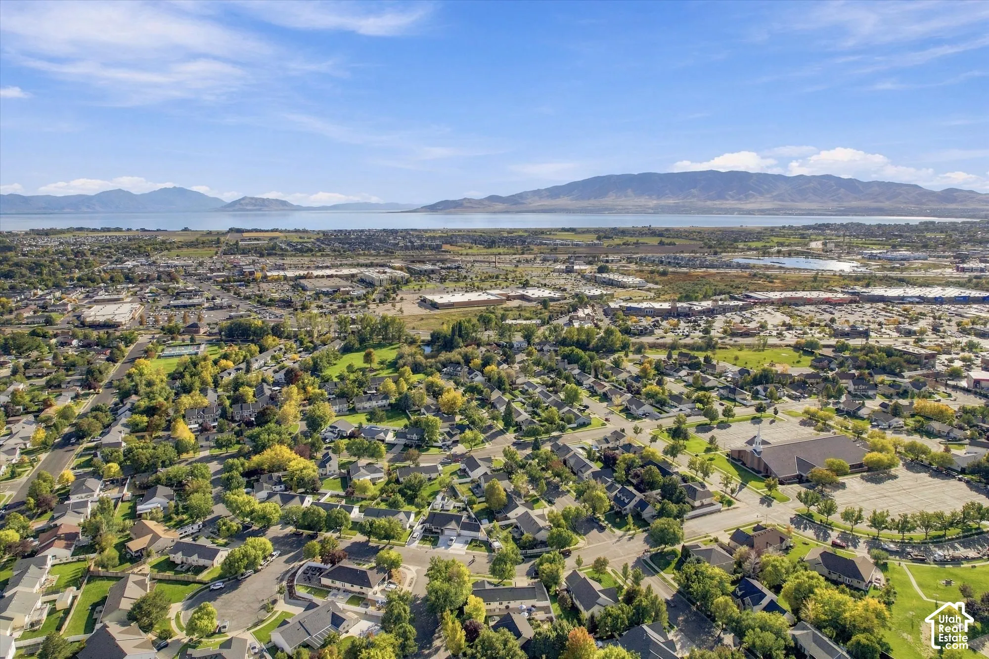 Aerial perspective showcasing a residential community with abundant mature trees and proximity to a large body of water, backed by distant mountains