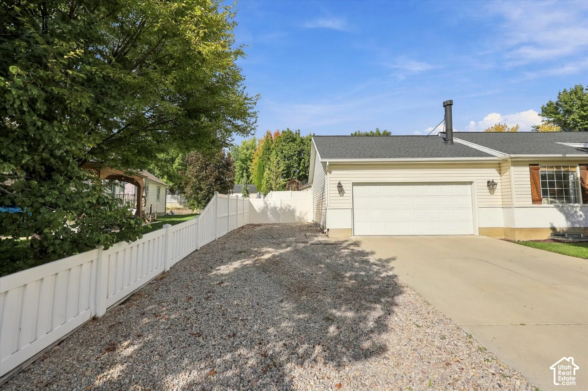 Attached two-car garage with a concrete driveway, white vinyl siding, dark shingle roof, and decorative window shutters
