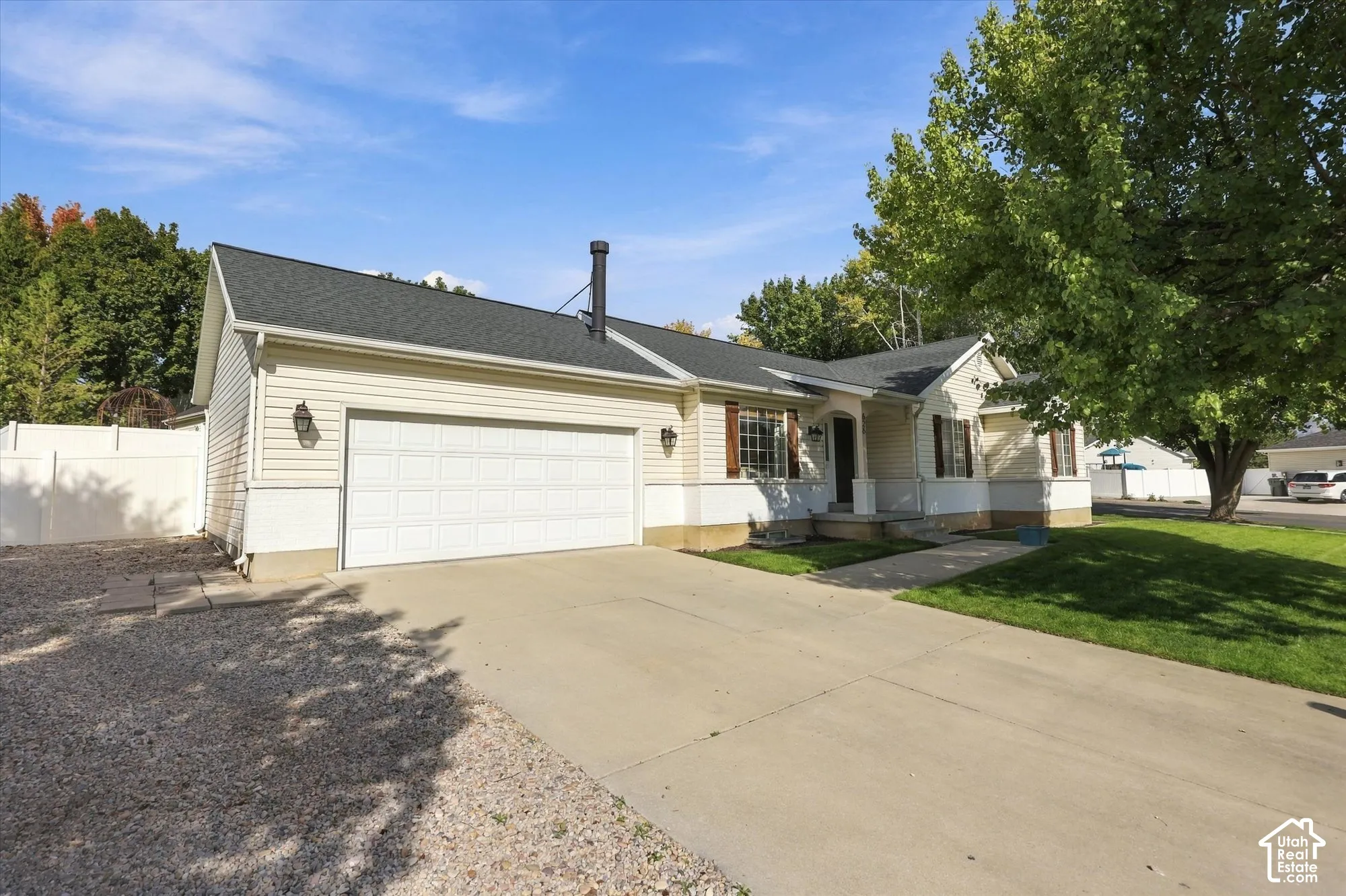 Cream-colored siding exterior, attached two-car garage, dark shingle roof, mature tree, and a concrete driveway