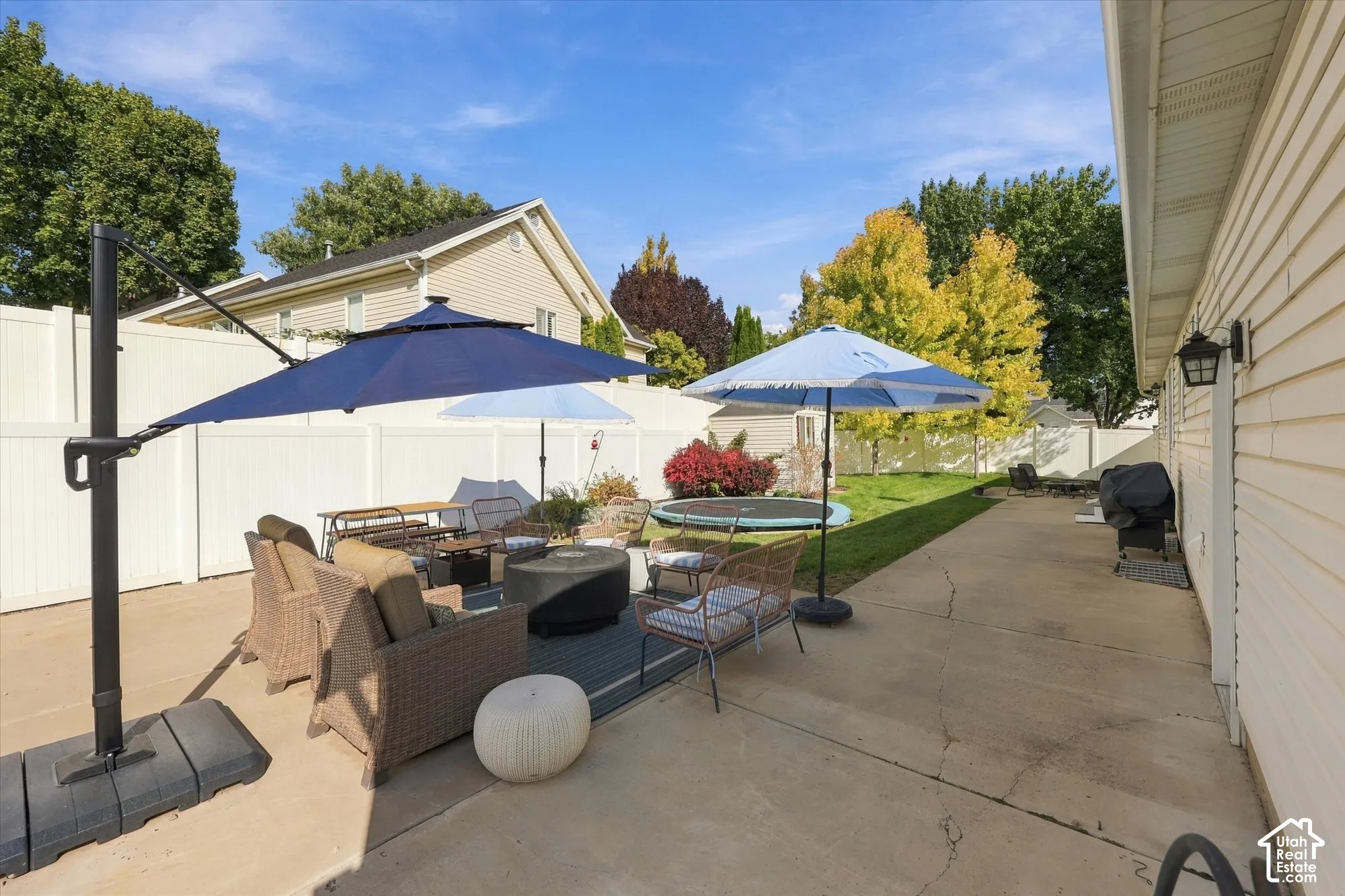 Expansive concrete patio with white privacy fencing, featuring an open lawn area and mature perimeter trees