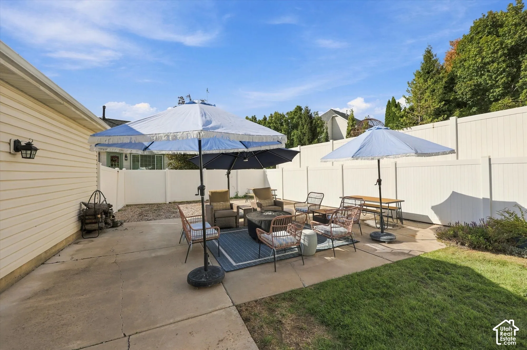 Expansive concrete patio with a fire pit, bordered by a white privacy fence and a manicured lawn