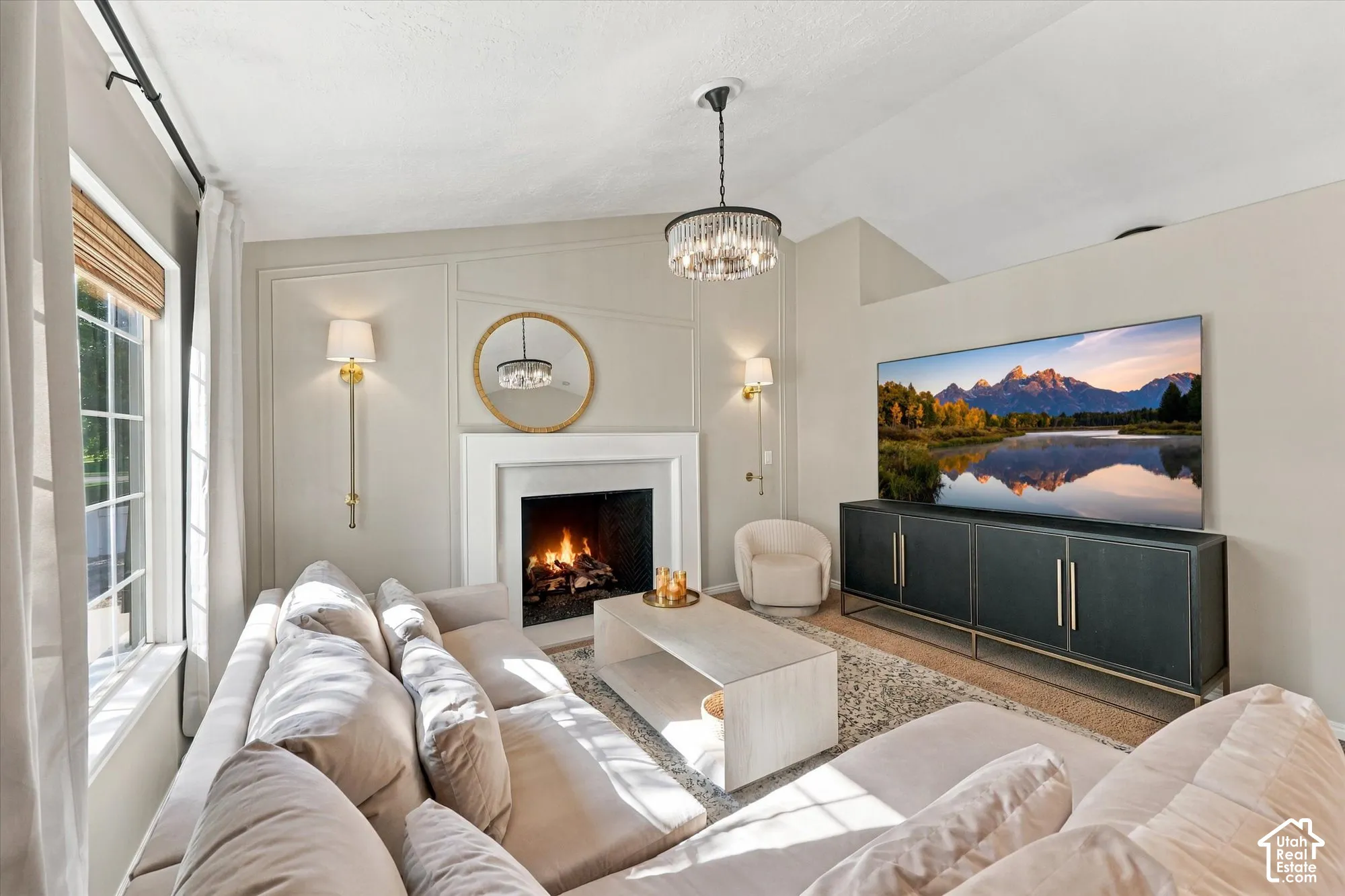 Vaulted ceiling with a crystal chandelier, fireplace with a white mantel, and panel accent wall