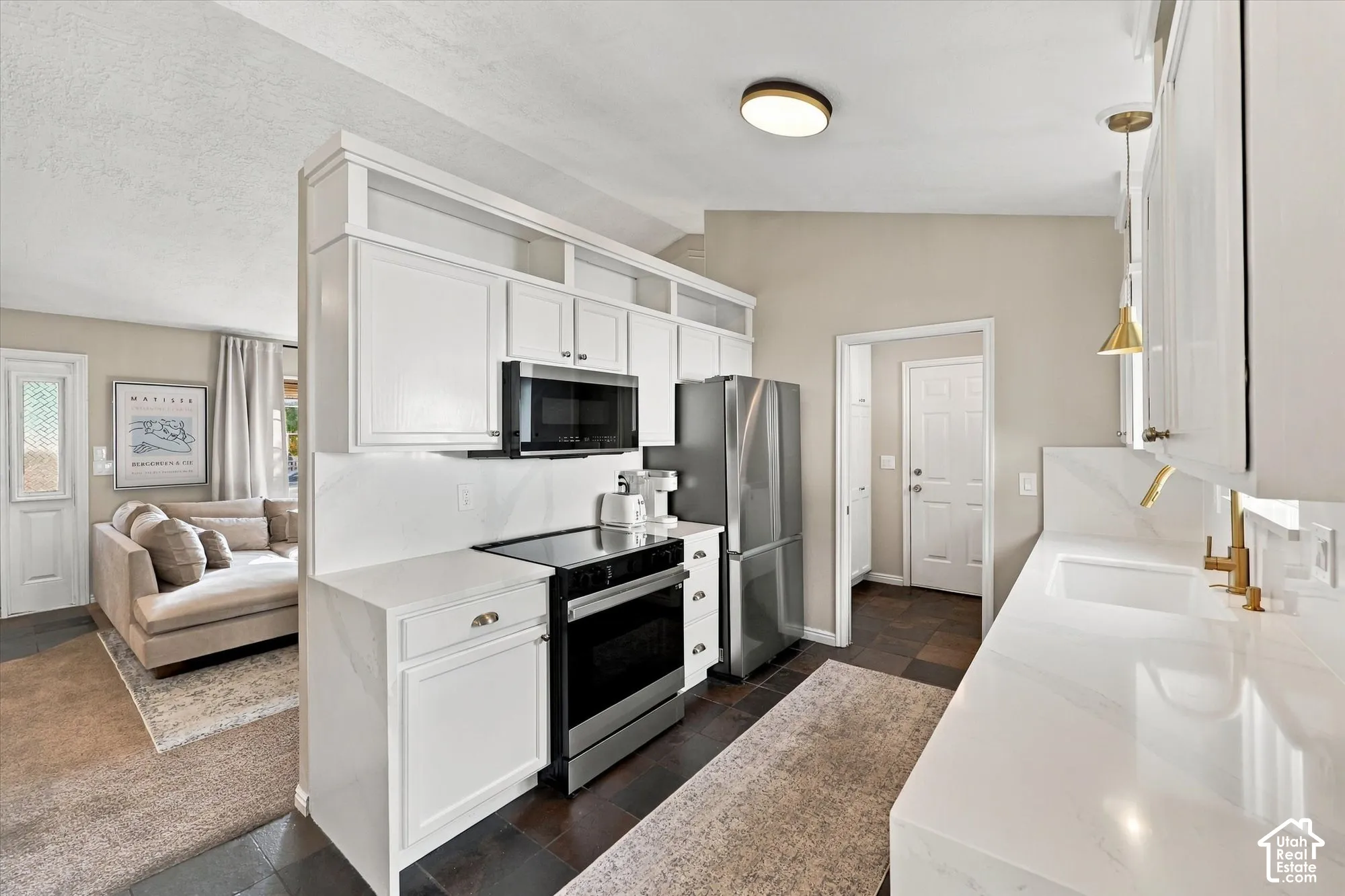 Kitchen featuring white cabinetry, stainless steel appliances, white countertops, and a gold-finish faucet