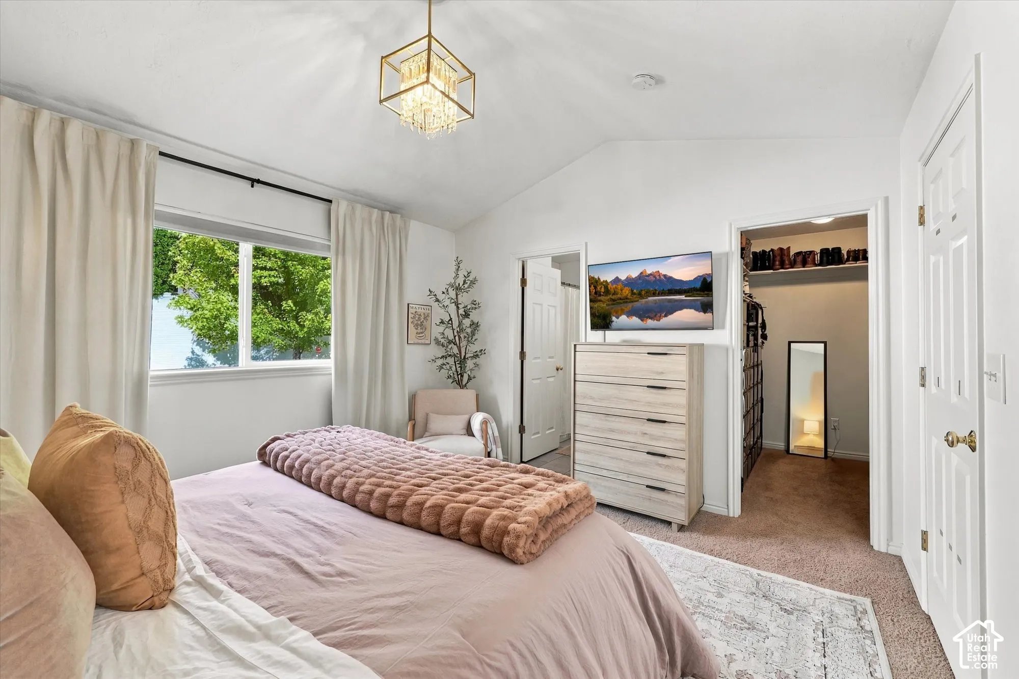 Vaulted ceiling with a contemporary chandelier, window with roller shade, and built-in closet storage