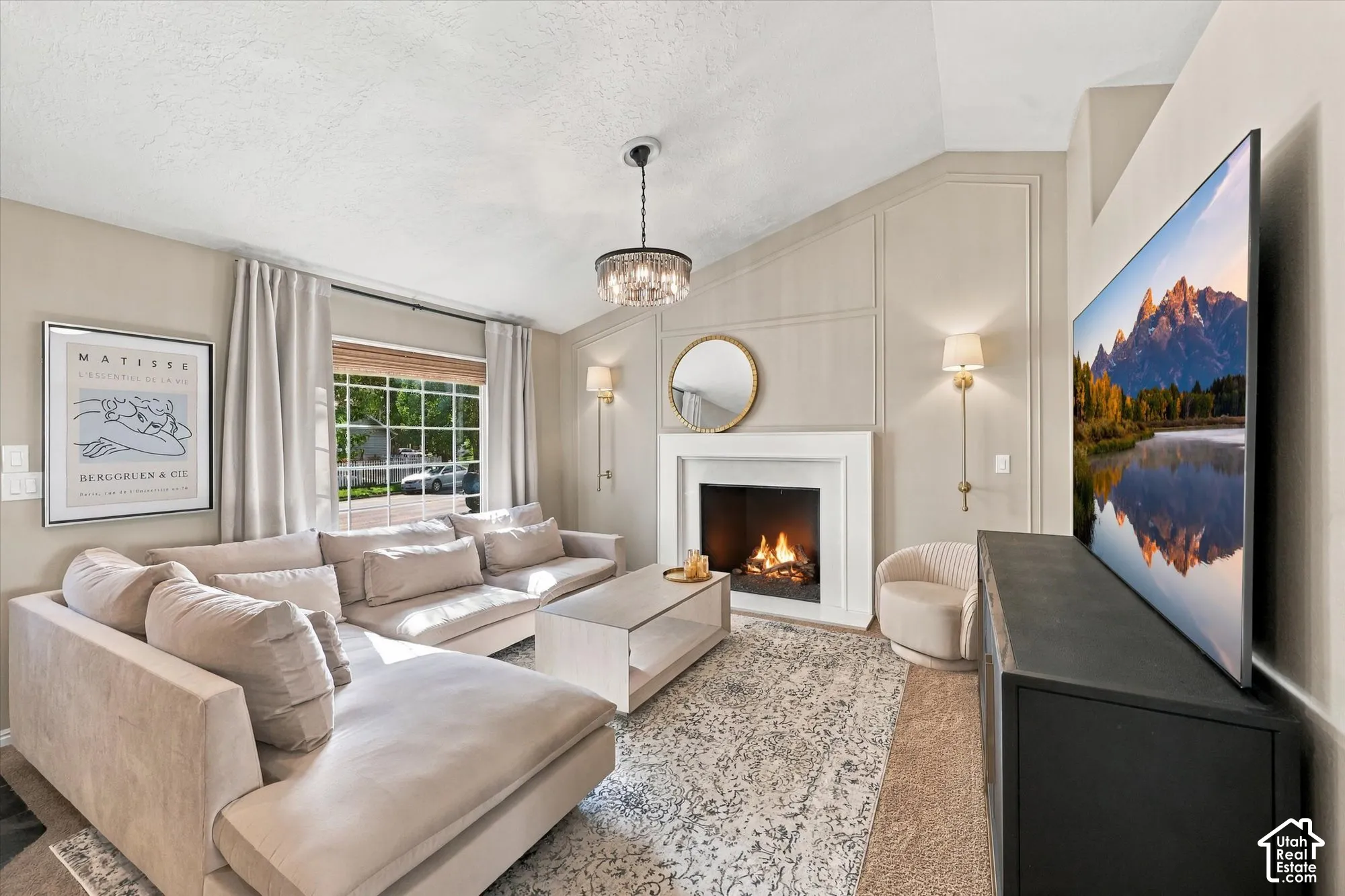 Vaulted ceiling with an elegant chandelier, a fireplace with a decorative mantel, and built-in wall paneling