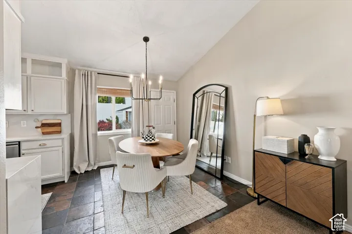 Vaulted ceiling with a black chandelier, white shaker-style cabinetry, white subway tile backsplash, and dark stone-finish flooring