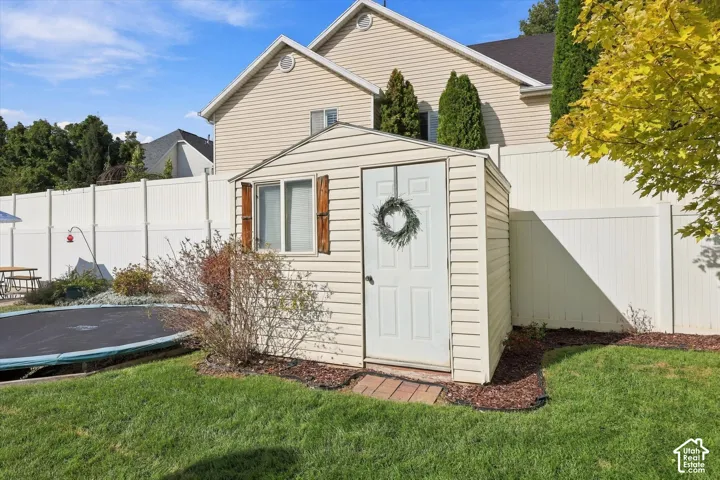Spacious backyard featuring a storage shed with wood-finish shutters, a vinyl privacy fence, and a manicured lawn